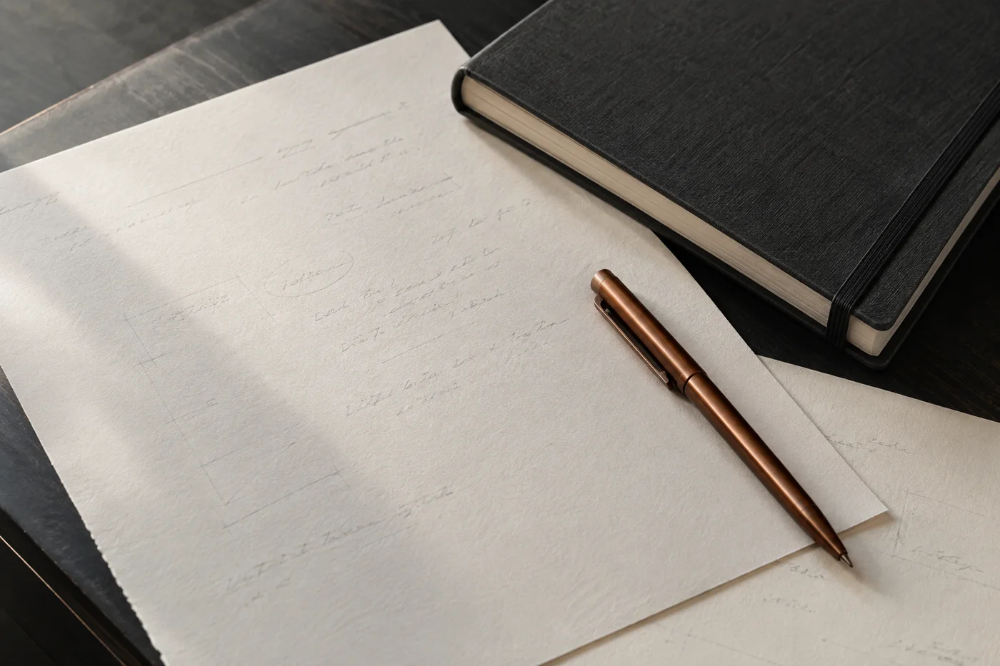 Planning notes, a copper pen, and a charcoal notebook
